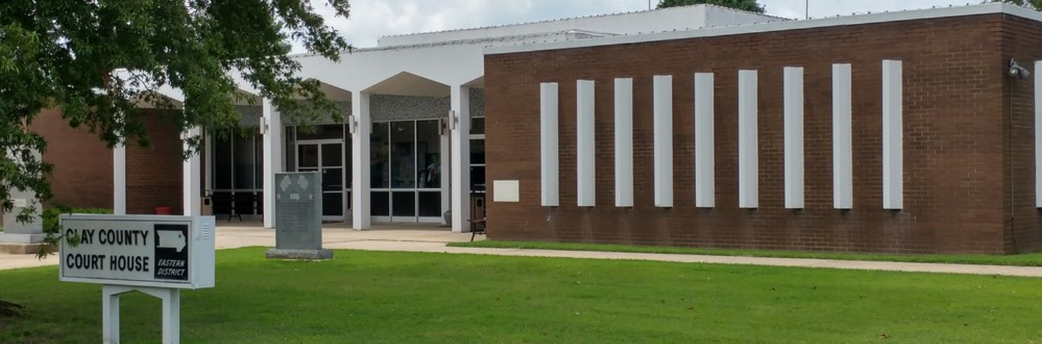Brick  building with white columns and a sign on a green lawn, under cloudy skies