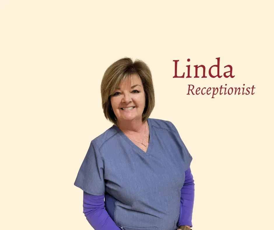 Smiling receptionist named Linda wearing blue scrubs.