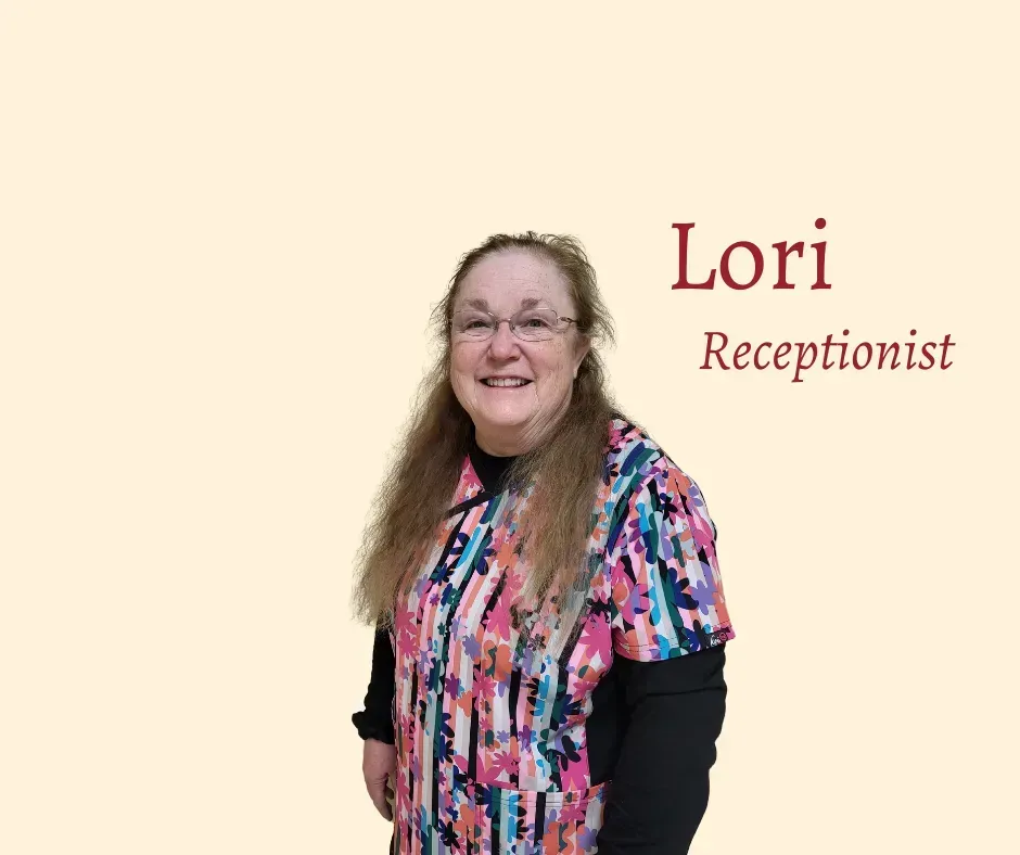 Lori, smiling receptionist, wearing patterned top, glasses. Standing against a light orange background.