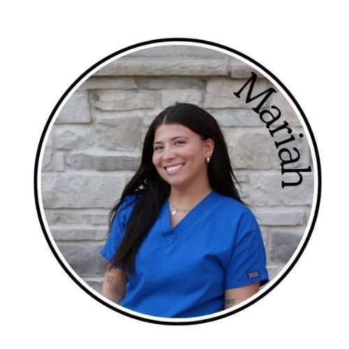 Woman in blue scrubs smiling in front of a stone wall, with “Mariah” written along the edge