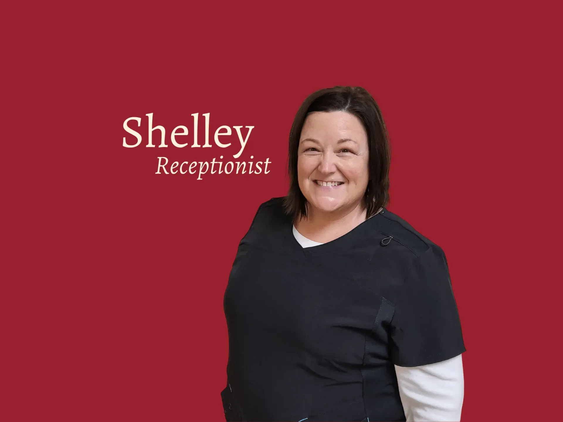 Shelley, a receptionist, smiles in front of a red background. She wears a black top over a white shirt.