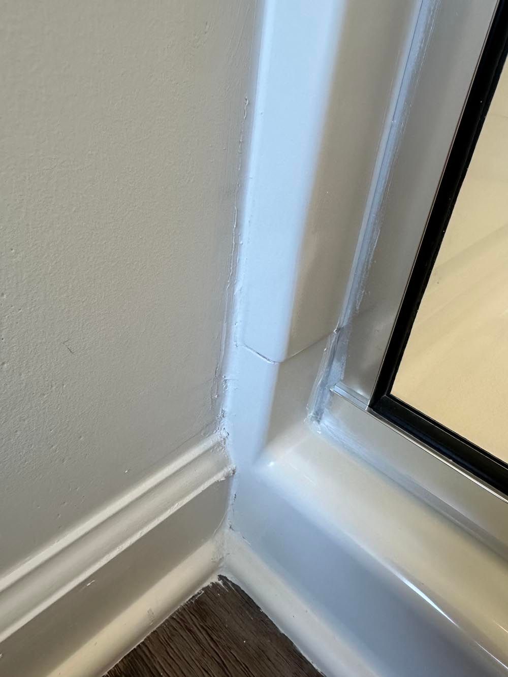 Corner of a white wall with molding and a window frame. Dark flooring visible.