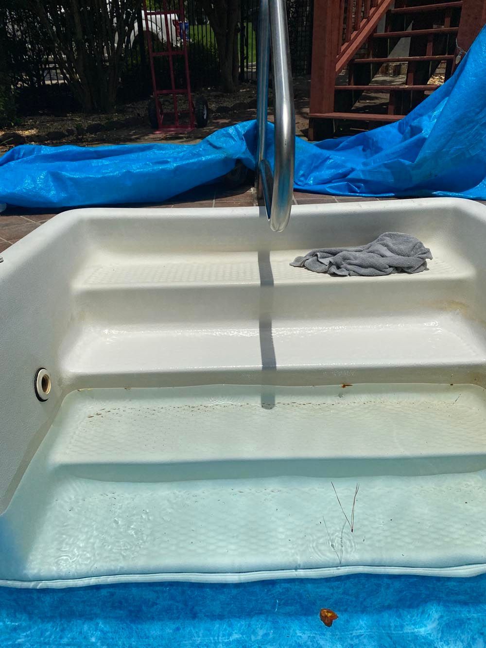 Pool steps with handrail, partially filled with water, and blue tarp.