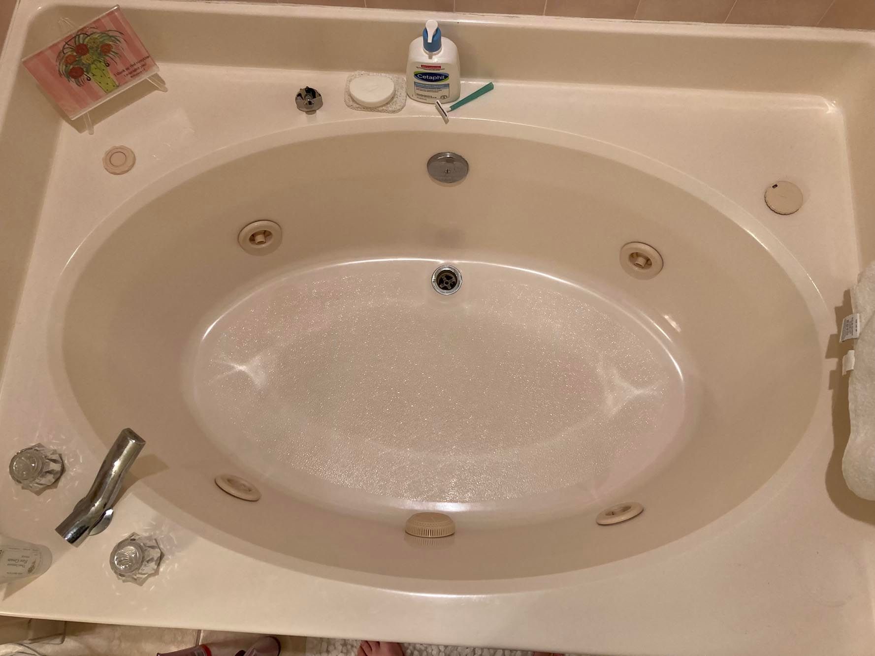 White oval jacuzzi tub with jets, soap, and a bottle of lotion.