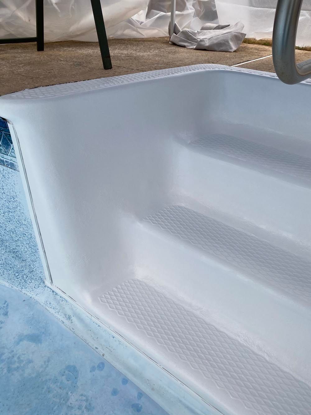 White pool steps leading into blue water, with a metal handrail.