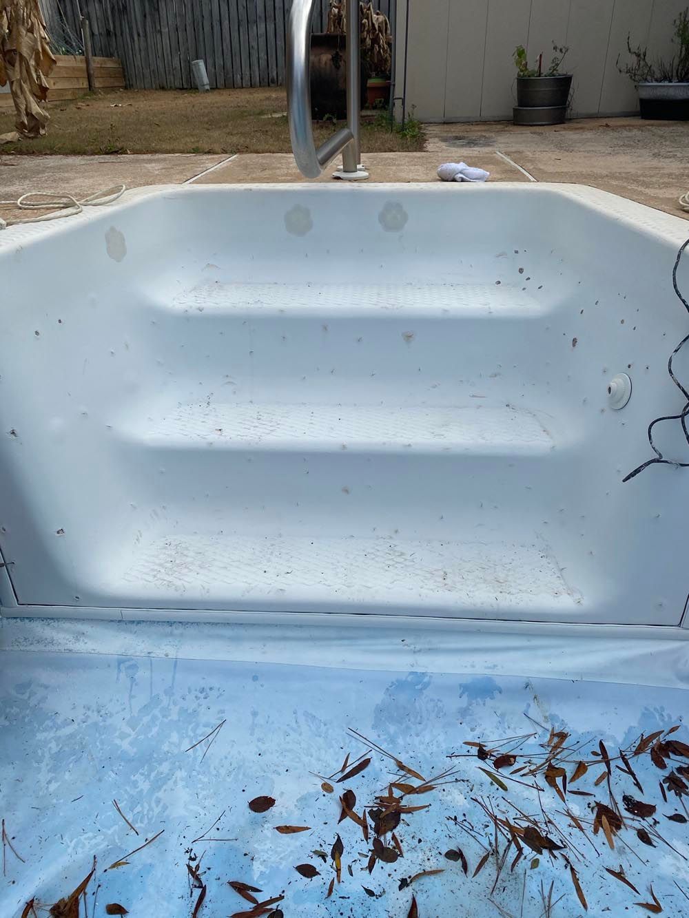 White hot tub with steps and debris inside.