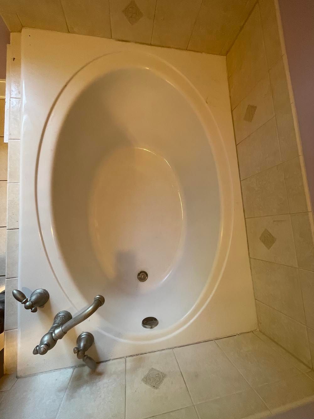 Oval-shaped white bathtub with silver faucet, set in a bathroom with tiled walls and floor.
