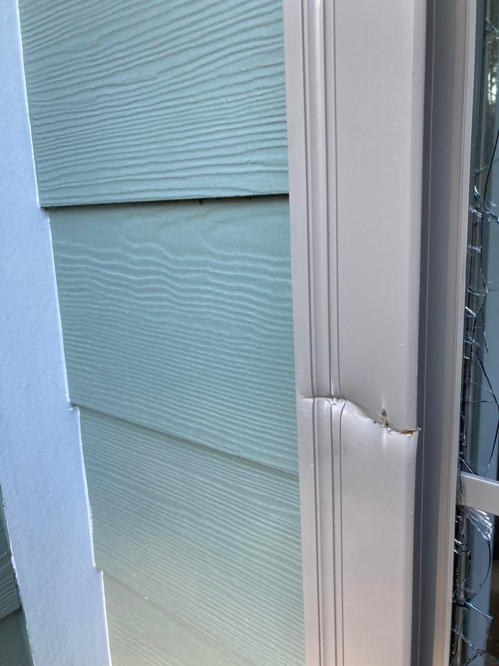 White window frame dented on light blue siding.