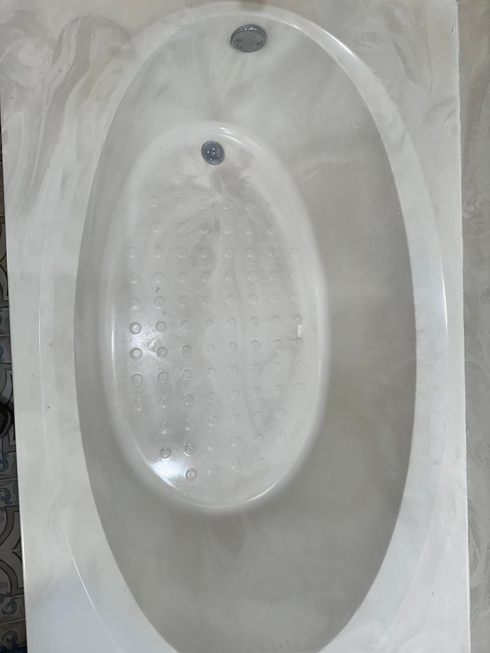 Oval-shaped white bathtub with bubbles, chrome fixtures. Marble-like surround.