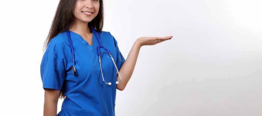 Smiling Asian nurse in blue scrubs holds her right hand out, palm up. White background.