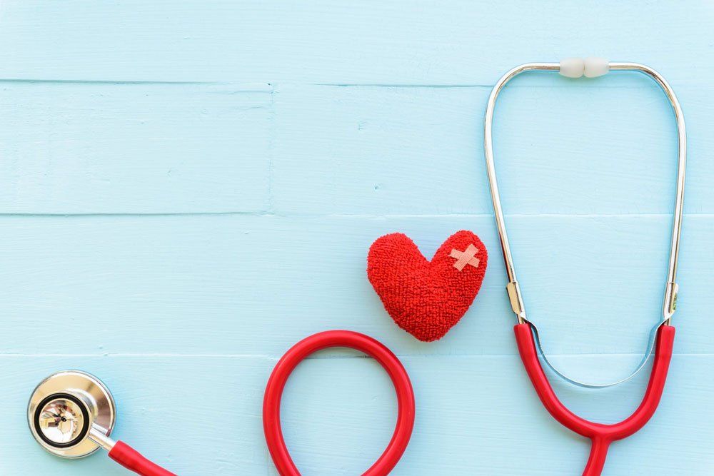 Red stethoscope next to a red heart with a bandage, on a blue wooden surface. Healthcare concept.