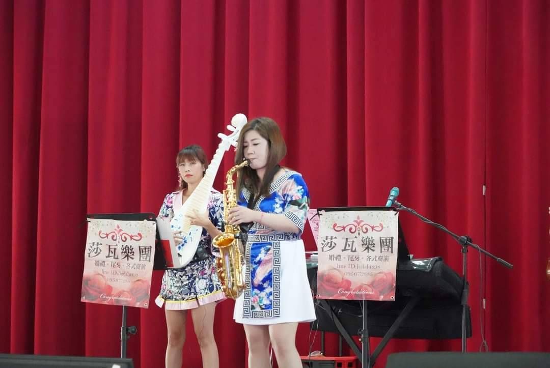 莎瓦舞台上兩名身穿藍色服裝的表演者，其中一人在紅色布幕前吹奏薩克斯風唱歌。