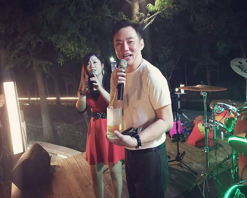莎瓦兩個人站在戶外舞台上，拿著麥克風唱歌，身後是鼓聲和綠色燈光。