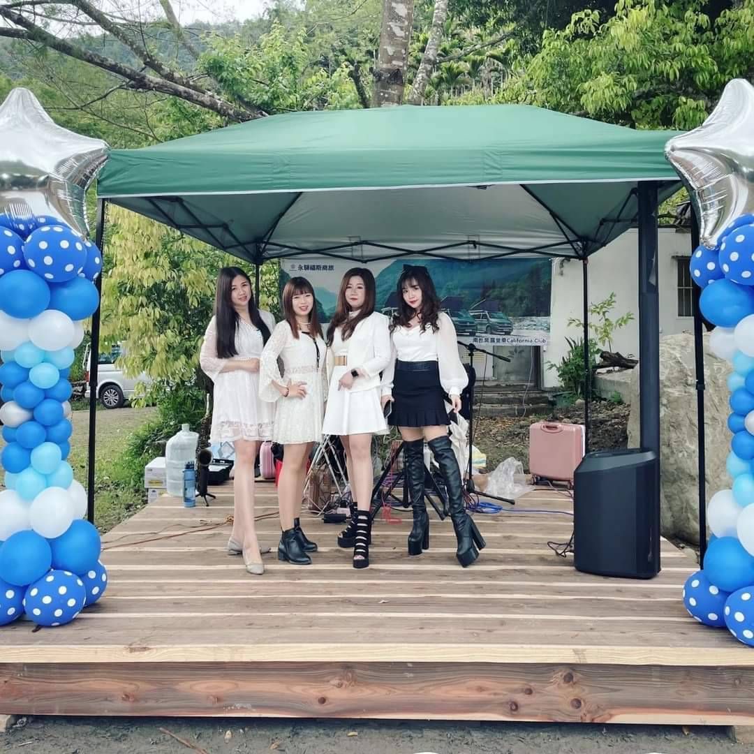 莎瓦四位女性在綠色天篷下的木製舞台上擺姿勢，周圍環繞著藍白相間的氣球柱。