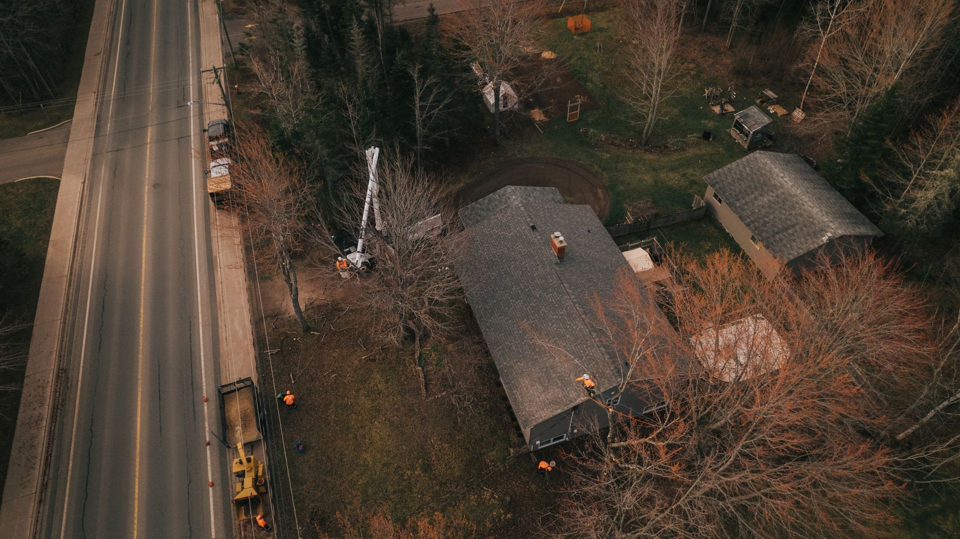 Aerial view: Construction equipment beside a road and a small house with workers on its roof.