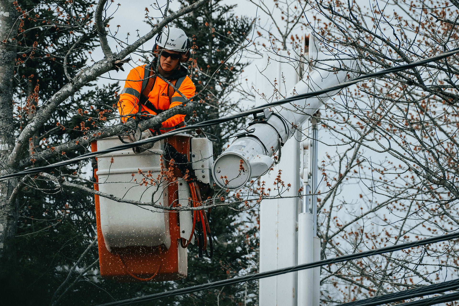 A man is sitting in a bucket on top of a power line.