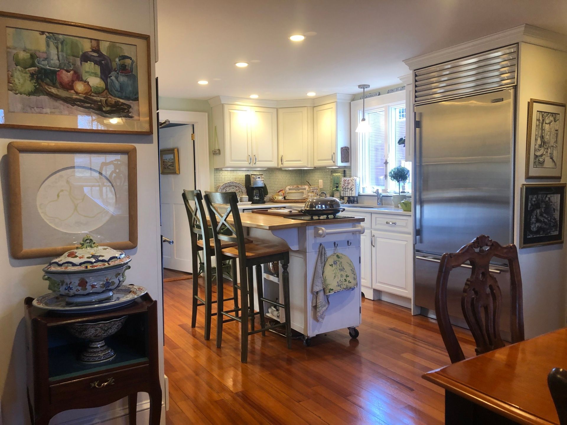 Kitchen with wood floors, white cabinets, island with stools, and stainless steel refrigerator.