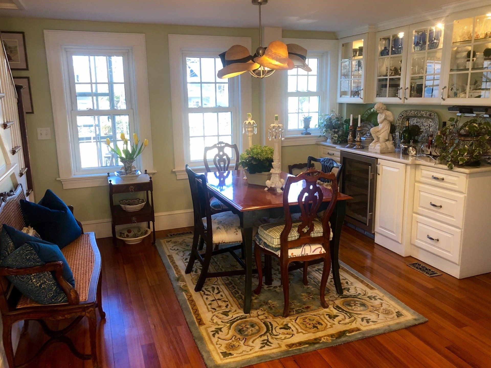 Dining room with wood floor, table, chairs, rug, cabinets, windows, and decorative items.