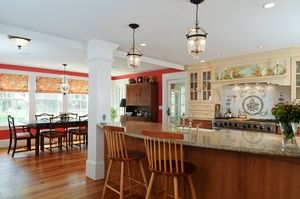 A kitchen with a large island and stools and a dining room in the background