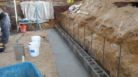 Construction site with concrete foundation and cinder block wall under construction.