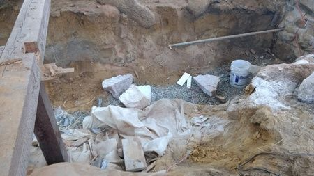 A pile of dirt and rocks in a hole with a wooden beam in the background.