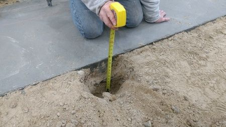 A person is measuring a hole in the ground with a tape measure.