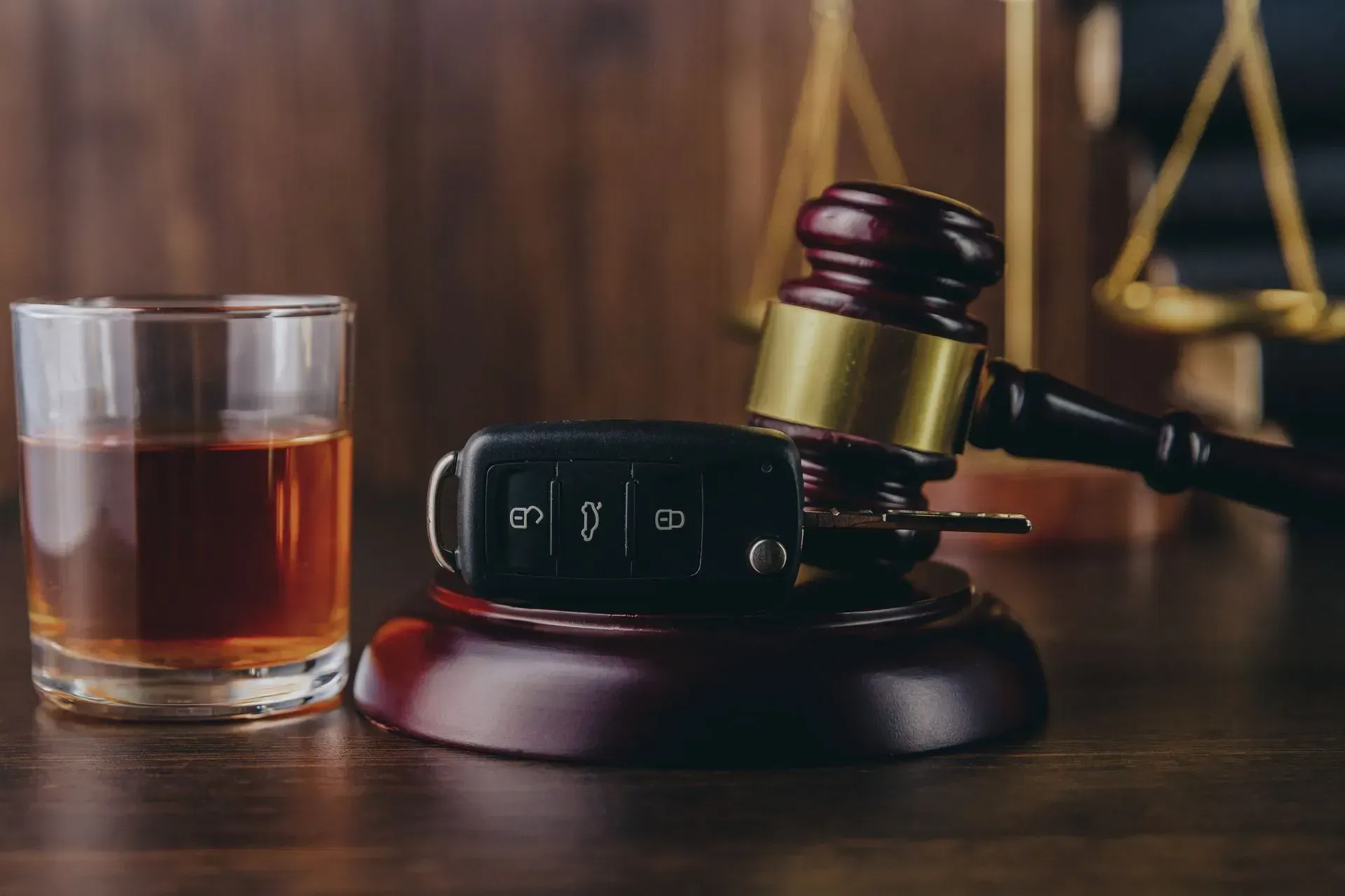 Judge’s gavel beside car key and whiskey glass on a wooden table