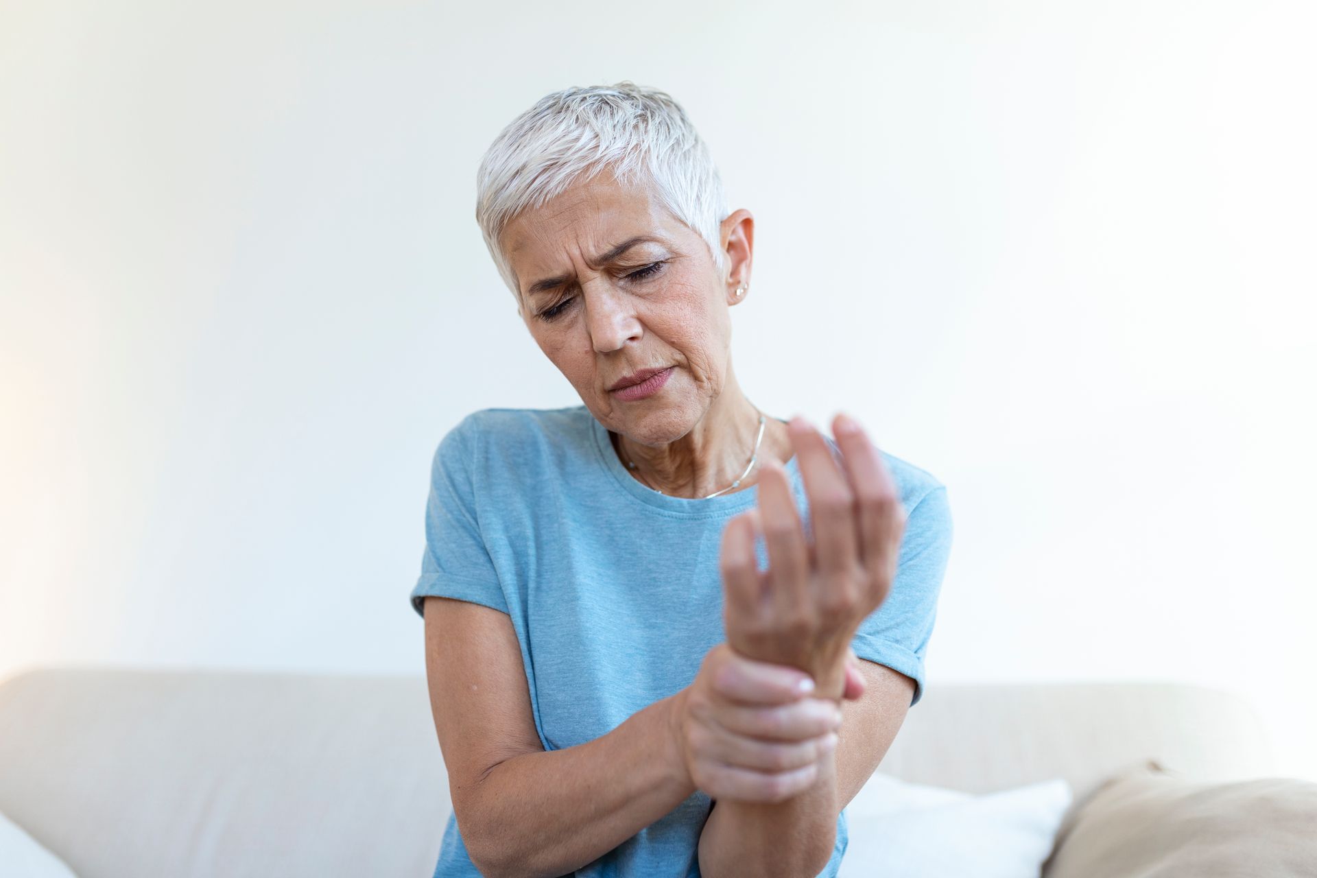 A person in a blue shirt holds their wrist and looks down with a concerned expression, indicating pain or discomfort.