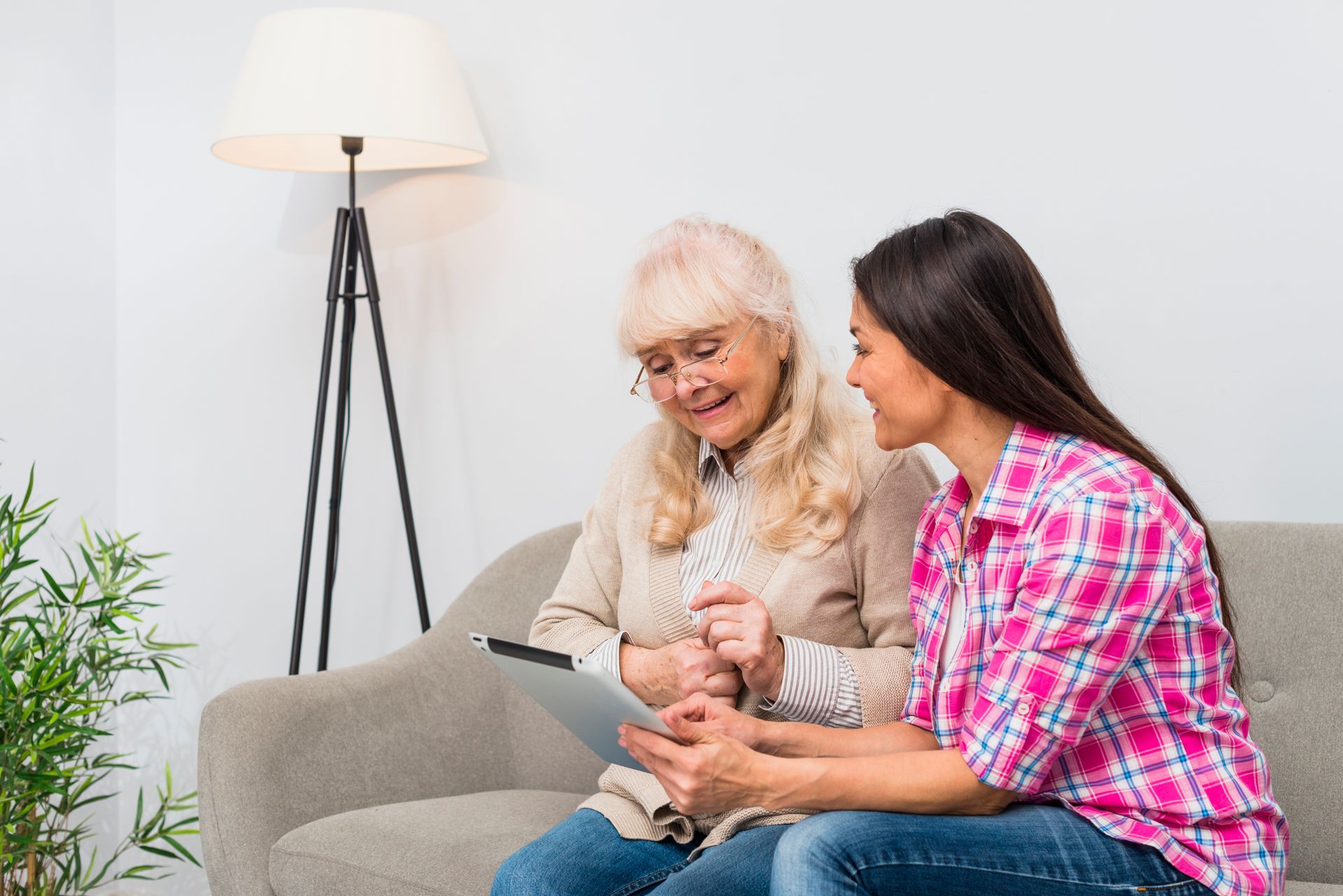 Two people sit on a sofa looking at a tablet together in a bright, modern room.