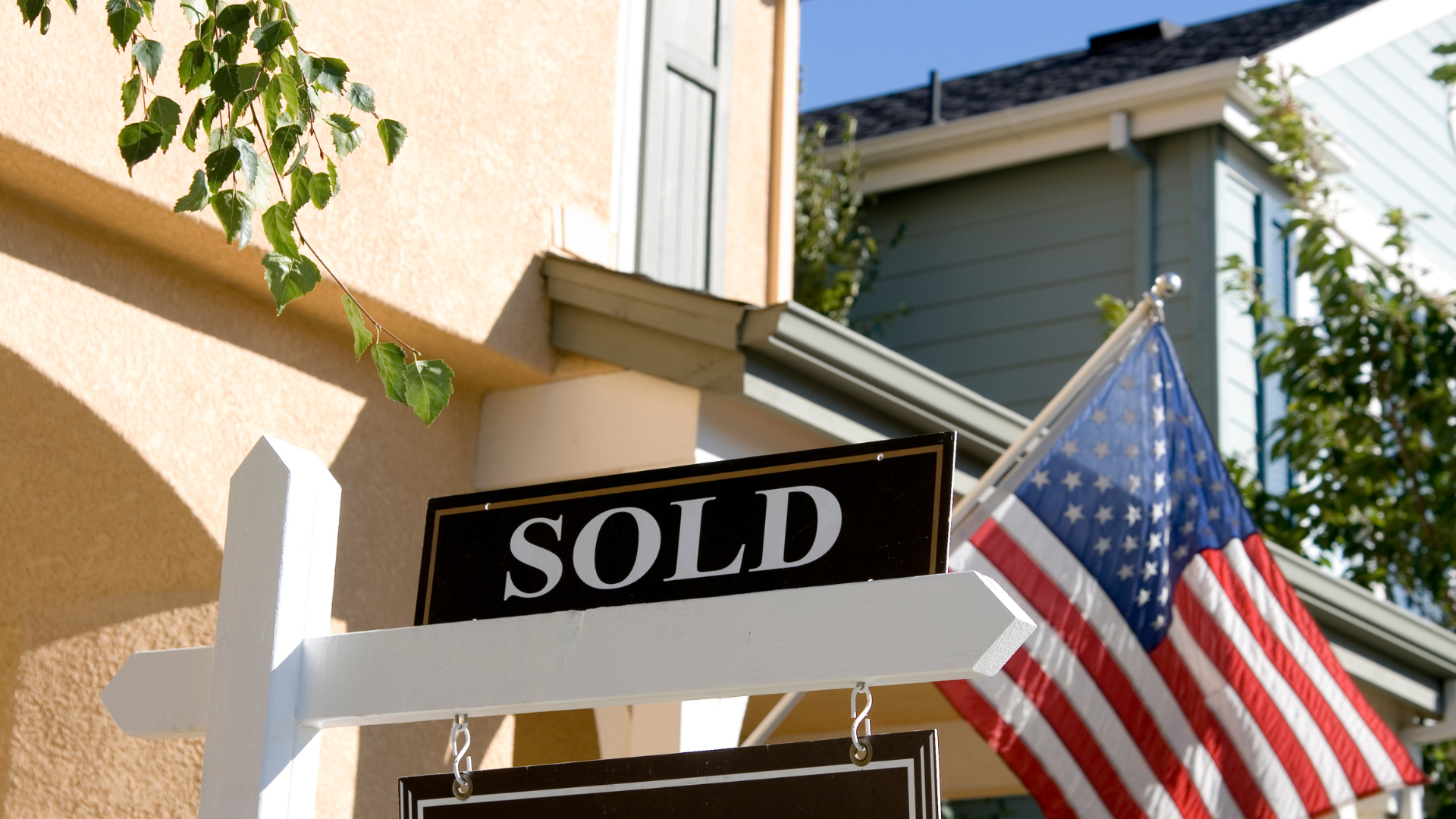 A sold sign with an american flag in front of a house