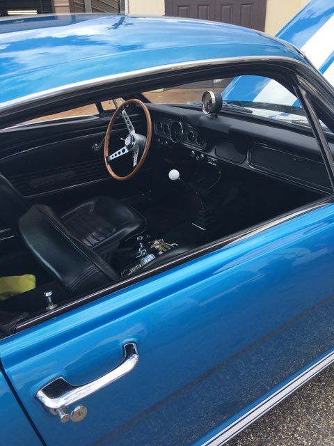 Blue vintage car with open window, showing black interior and wood-rim steering wheel
