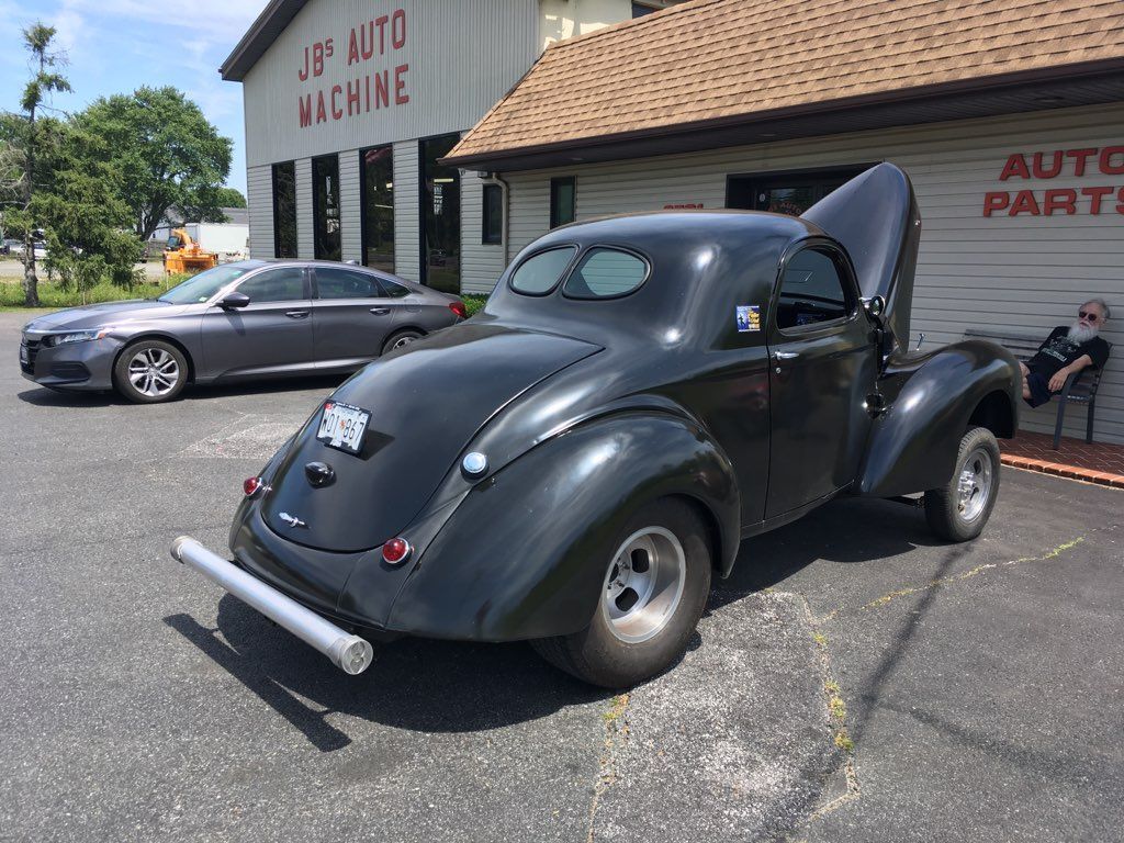 Black vintage hot rod with open hood parked outside an auto parts shop