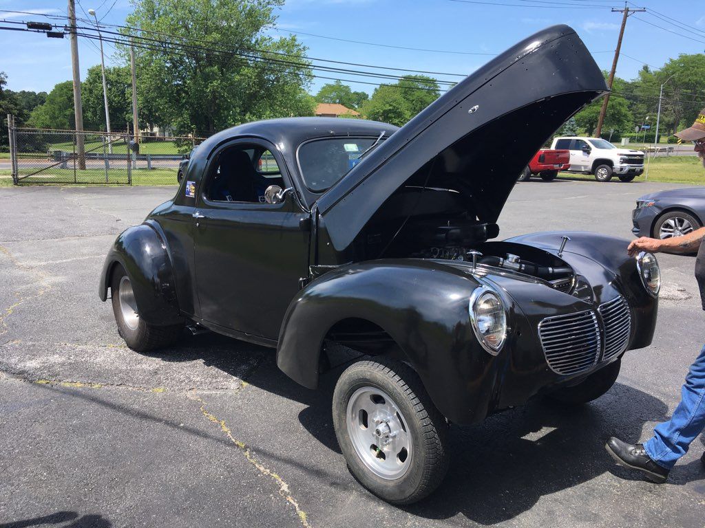 Black vintage car with hood open in a parking lot, with a person standing beside it