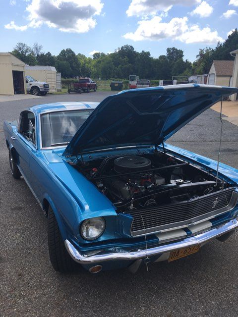 Blue classic car with hood open, showing engine in a parking lot