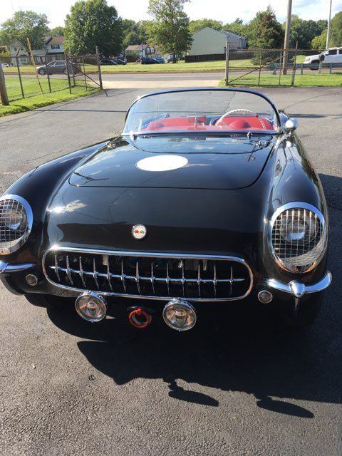 Black vintage Corvette with red interior, white racing circle, and front fog lights.