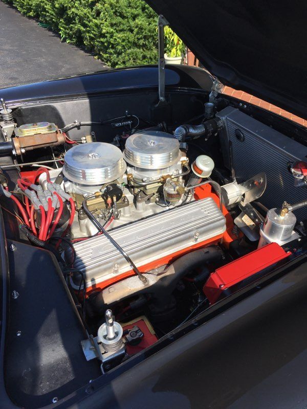 Black car engine with two silver carburetors, red wires, and a black open hood.