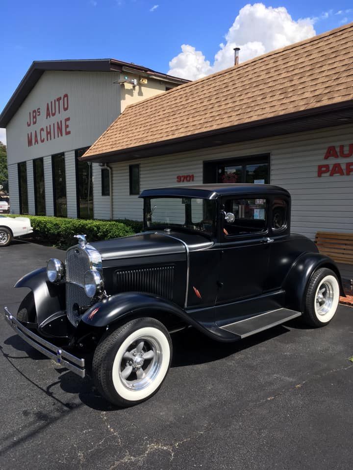 Black vintage car with white-wall tires parked in front of a building labeled 