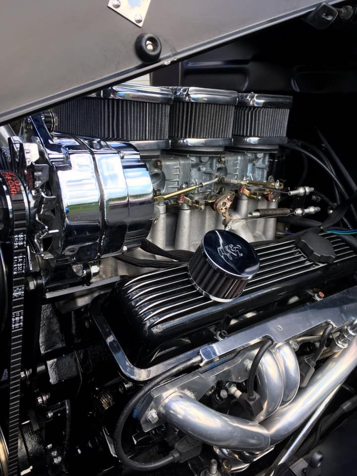 Chrome-detailed hot rod engine with triple carburetors, shiny chrome alternator, and black engine components.