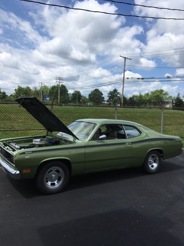 Green vintage car with hood open, parked outdoors under a cloudy sky.