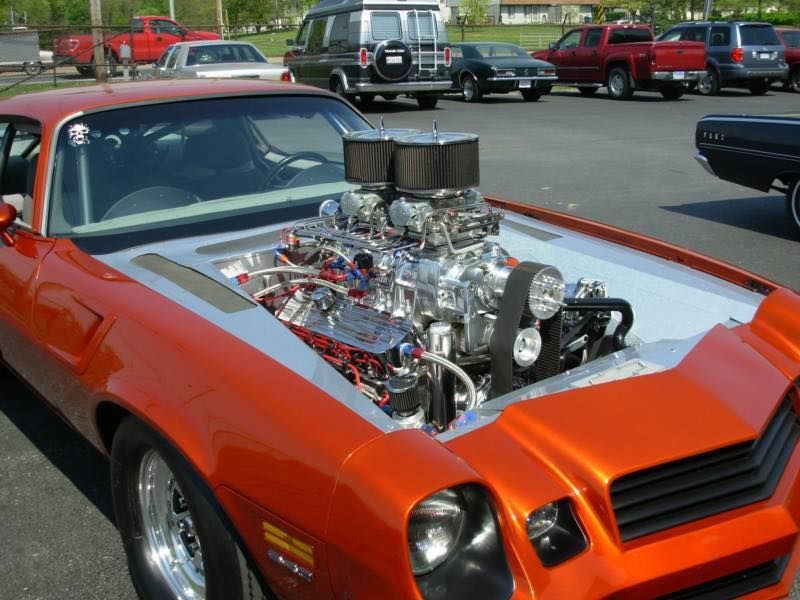Orange muscle car with exposed, powerful engine; parked in a lot.