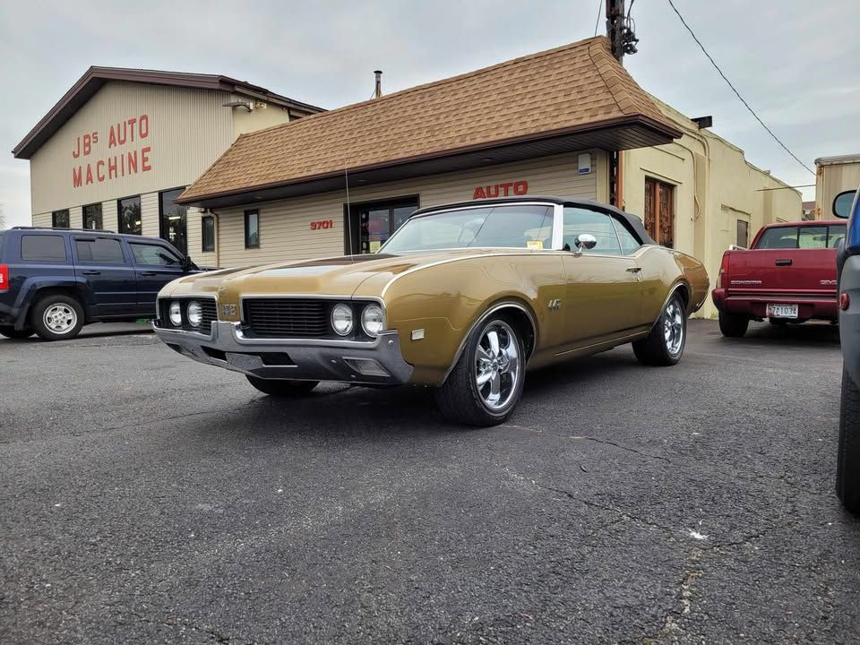 Gold convertible classic car parked in front of J&J Auto Machine shop on a paved lot.