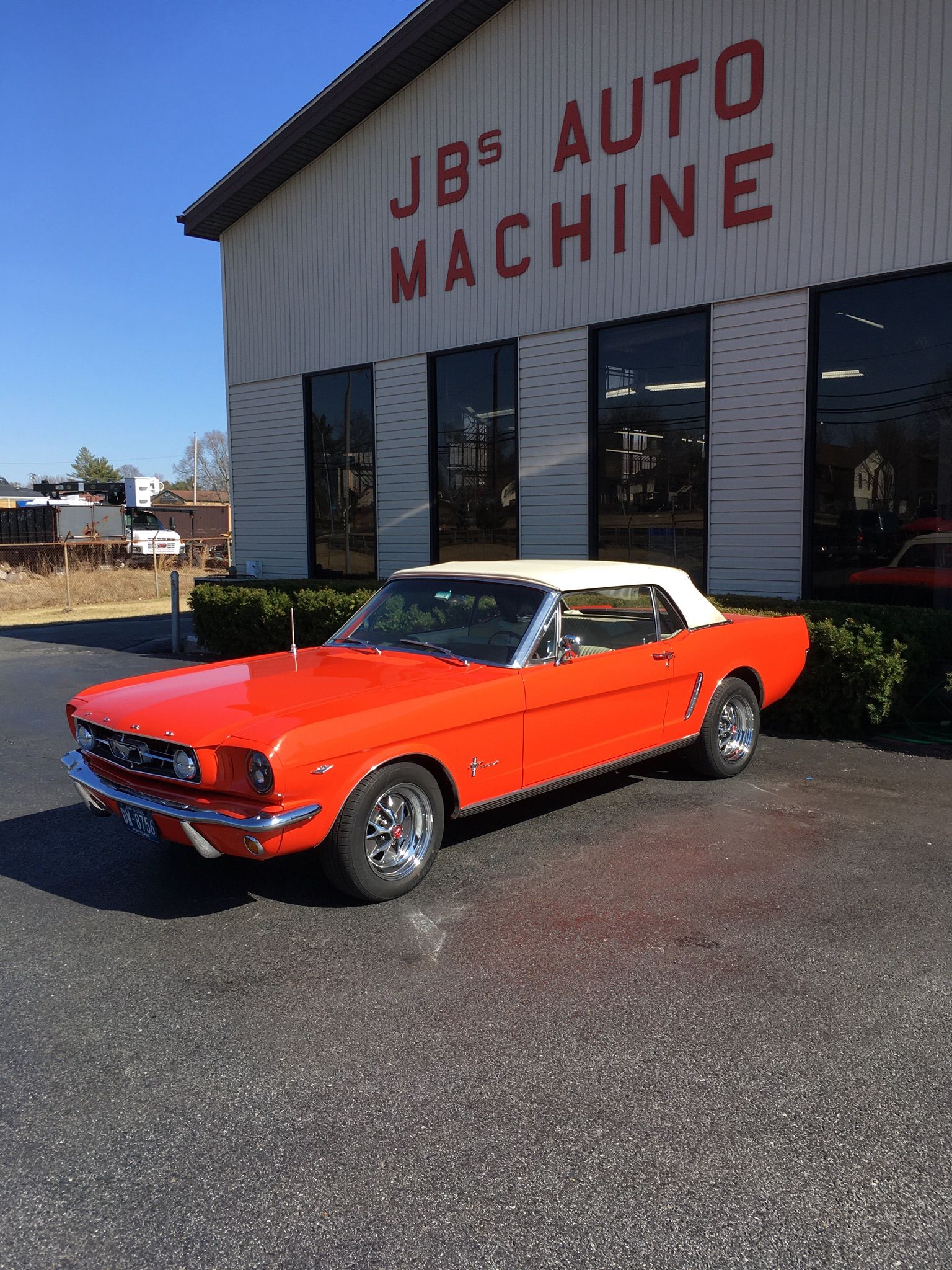 Red convertible Mustang parked outside JB's Auto Machine building on a sunny day.