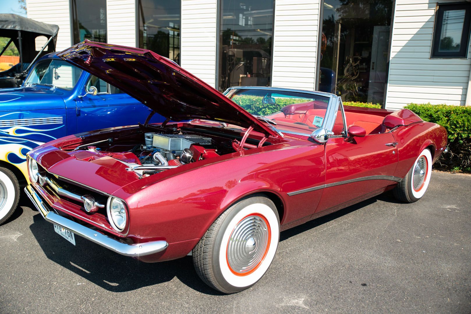 Red convertible classic car with hood open and whitewall tires.