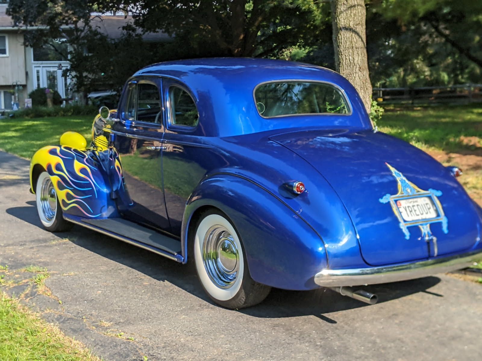 Blue custom classic car with flames parked on a driveway.