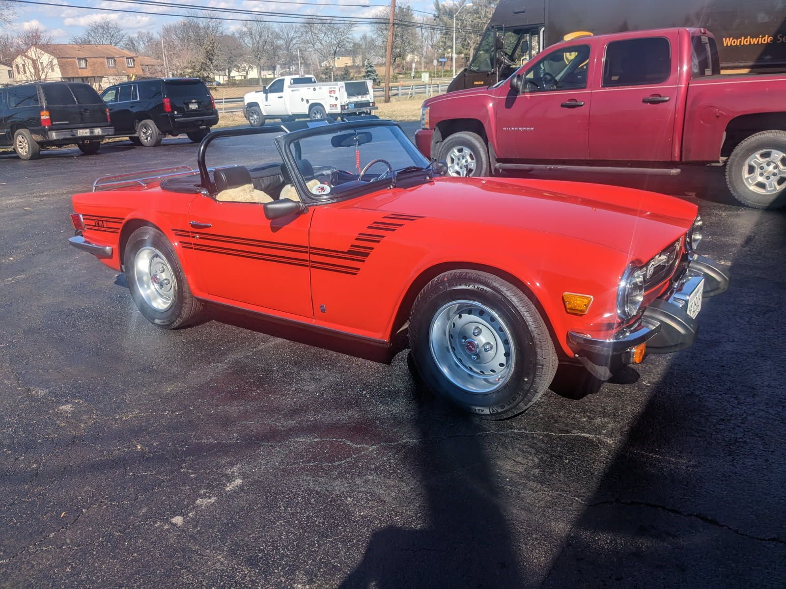 Red Triumph TR6 convertible with black graphics, parked outdoors.