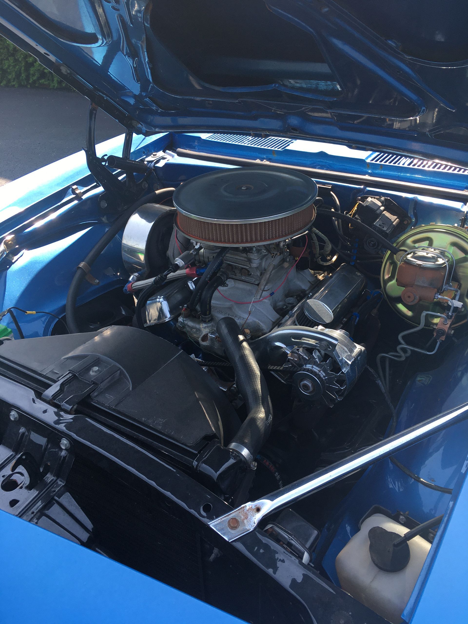 Blue classic car engine bay with black engine components and a chrome air filter.