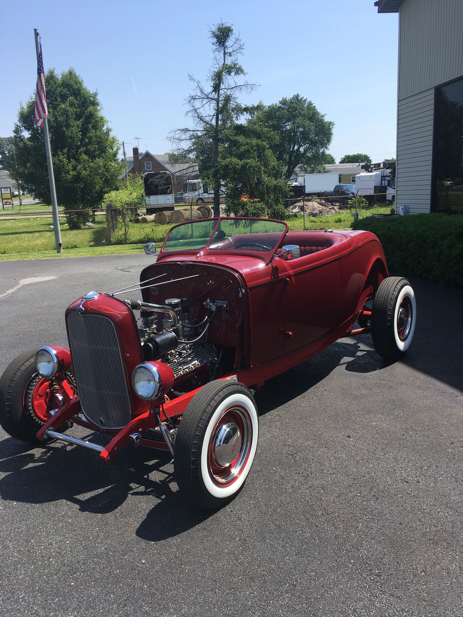 Red hot rod with white-walled tires, parked outside under a blue sky.