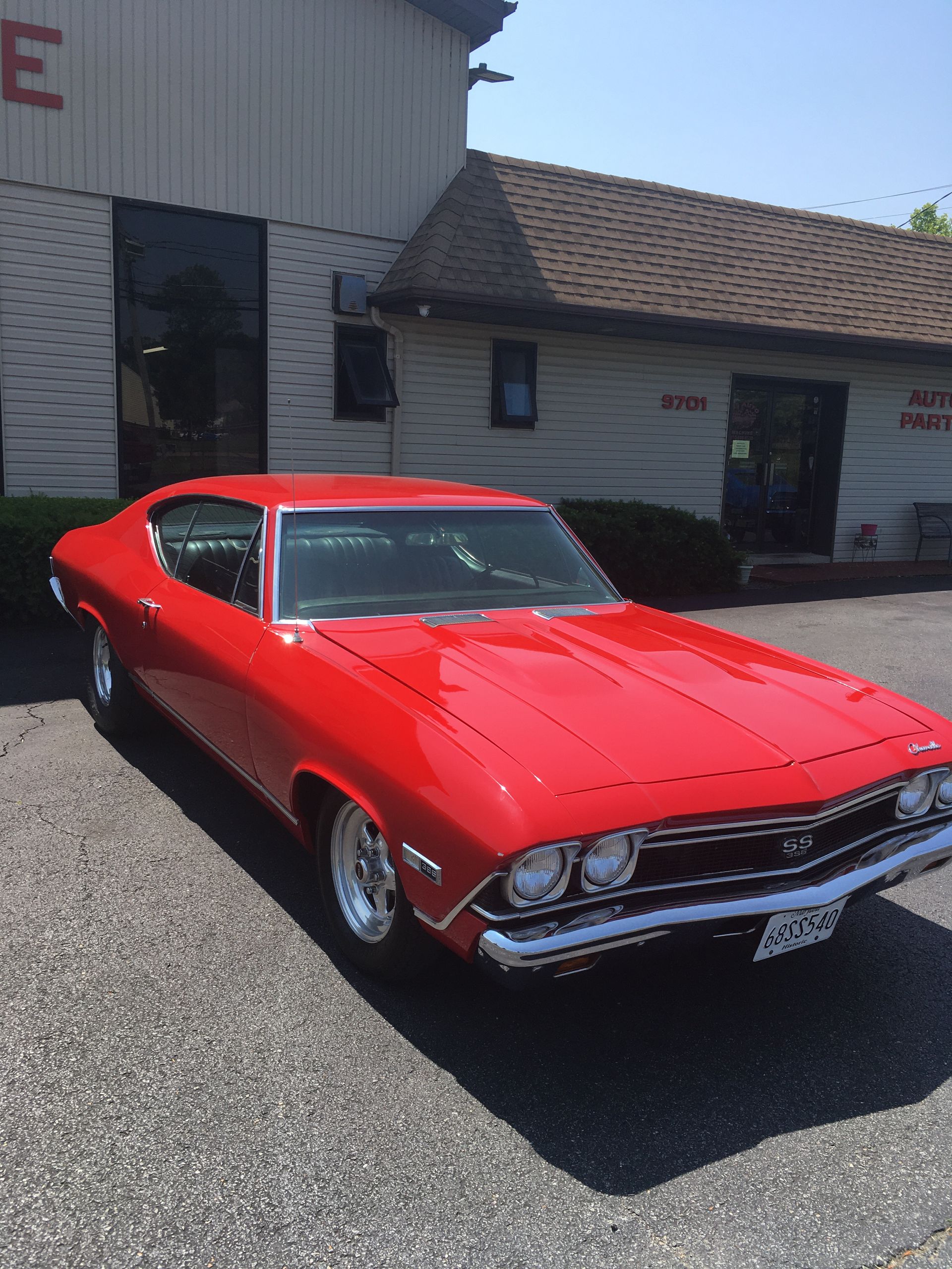 Red classic muscle car parked in front of a building with a gray asphalt parking lot.
