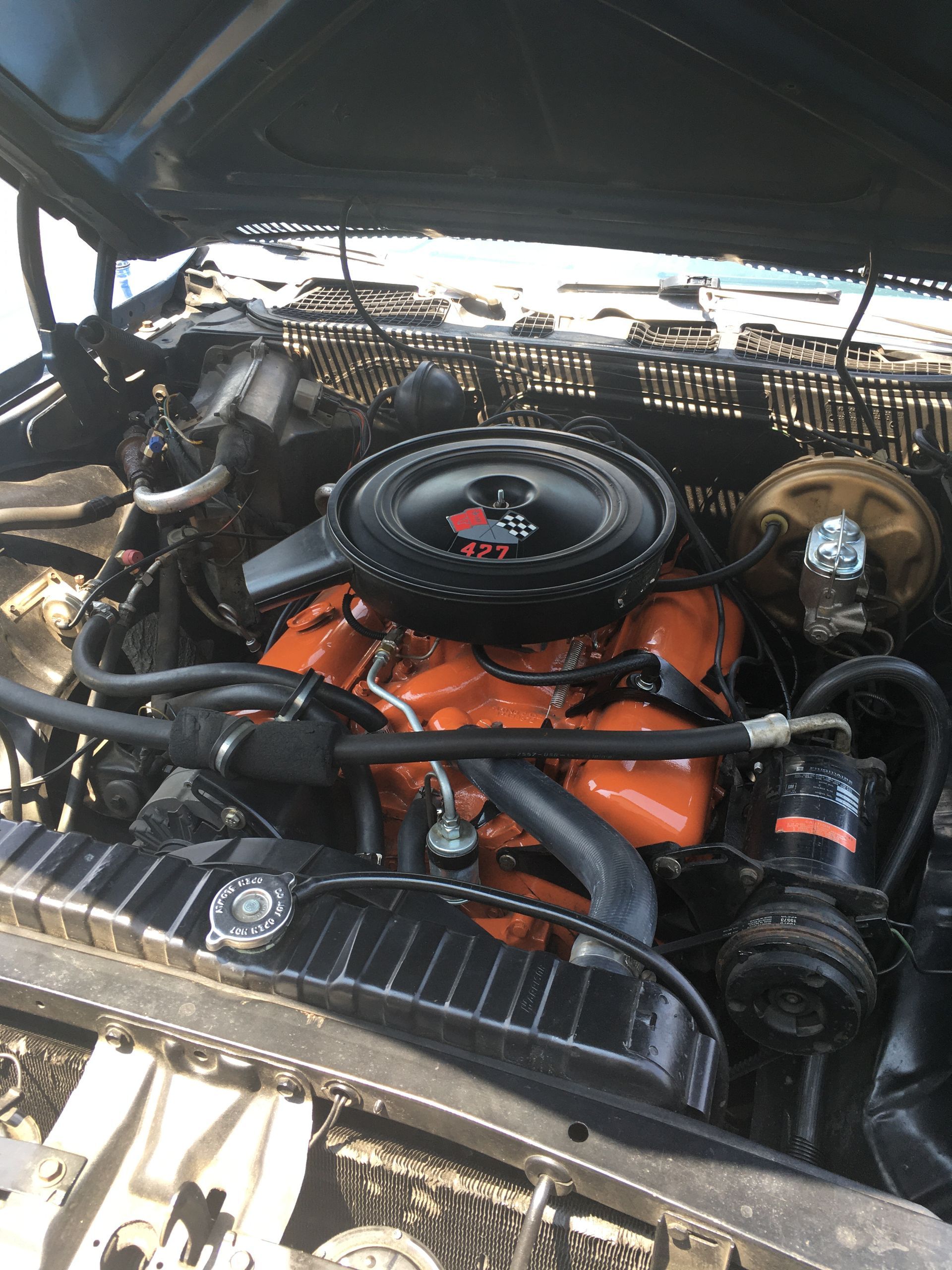 Orange engine in a classic car, with black air filter and surrounding engine components.