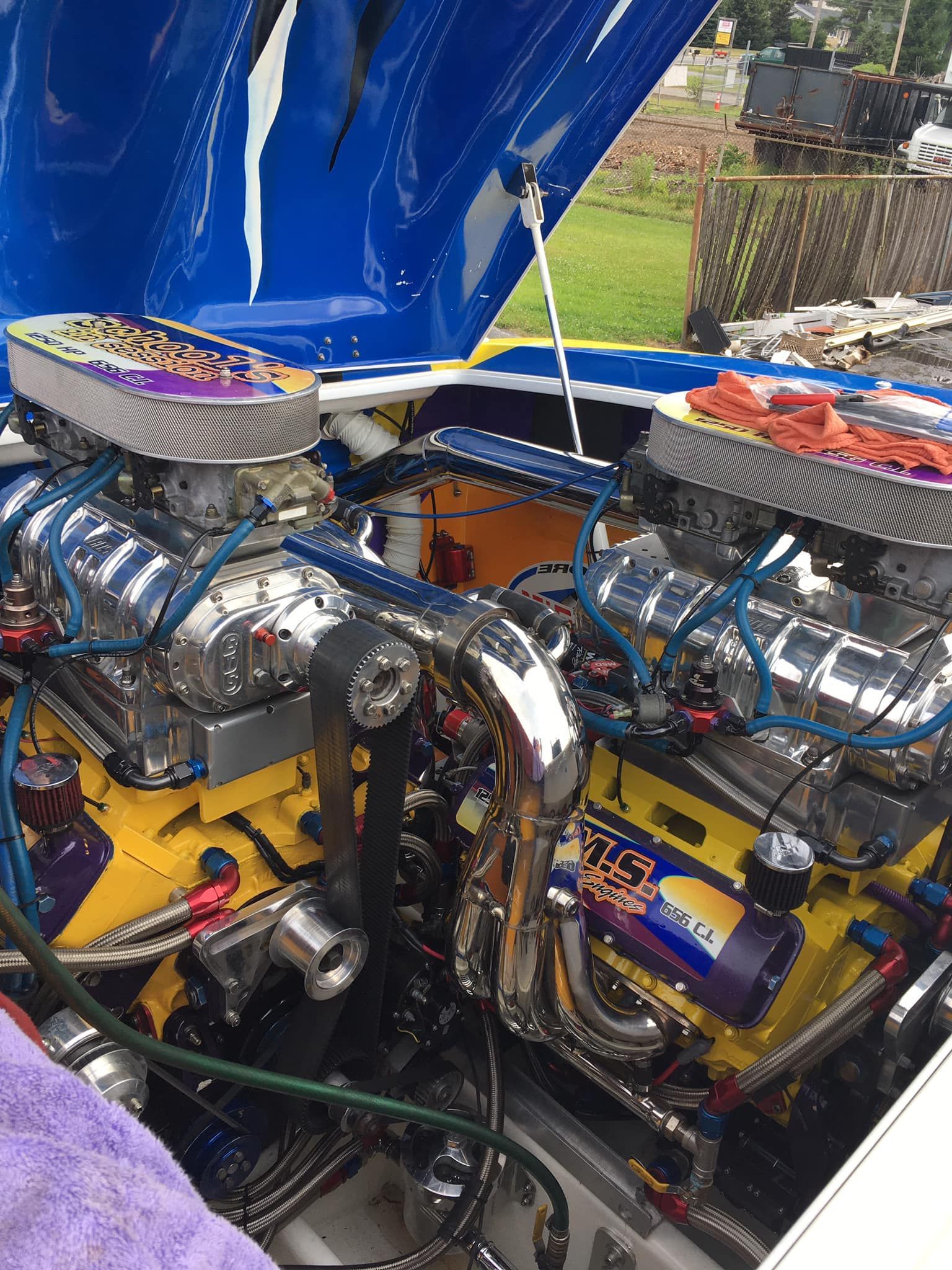 Two chrome boat engines, yellow and blue accents, under a blue and white boat hood.